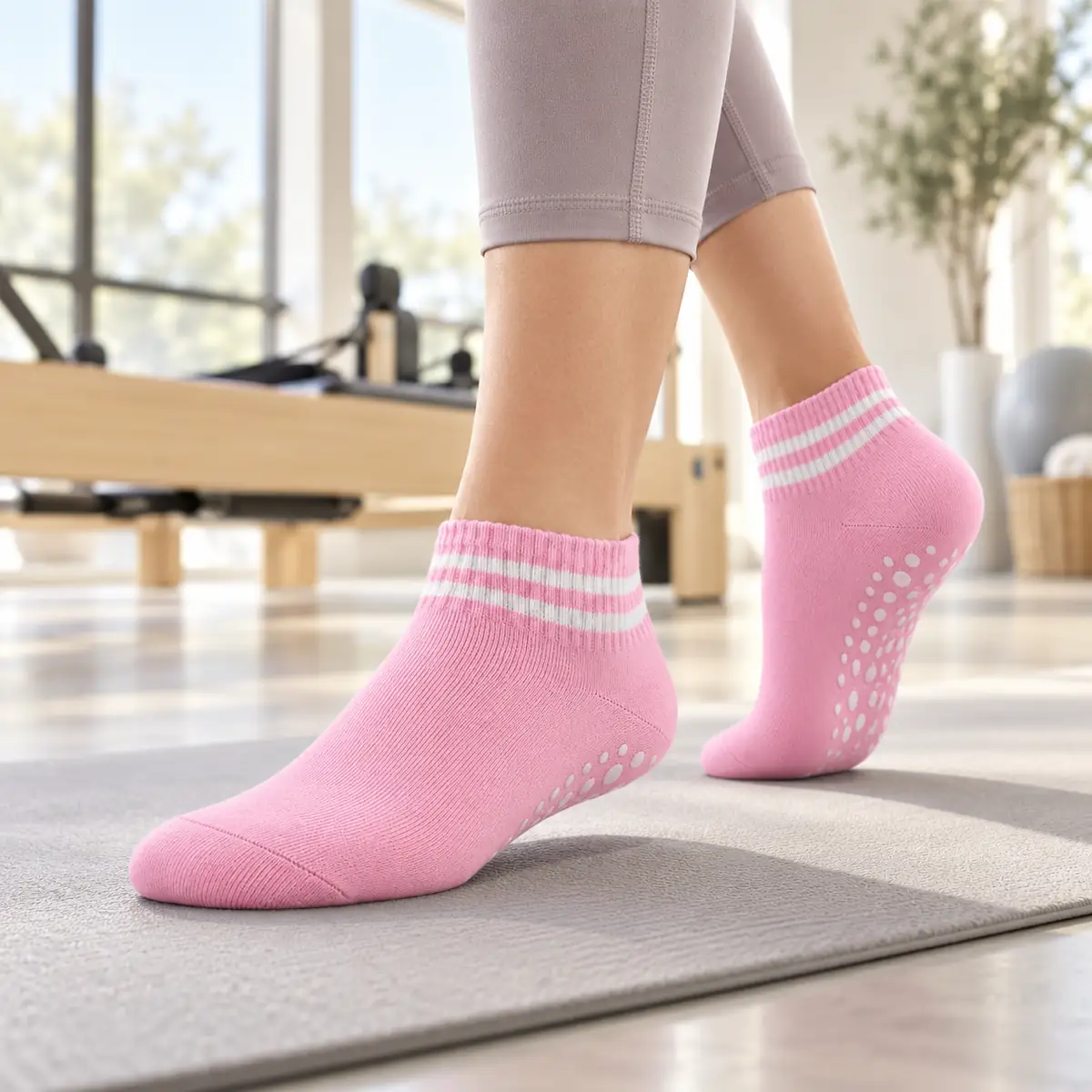 Pink PIVELYA ankle grip sock worn on a mat in a bright Pilates studio, reformer out of focus behind